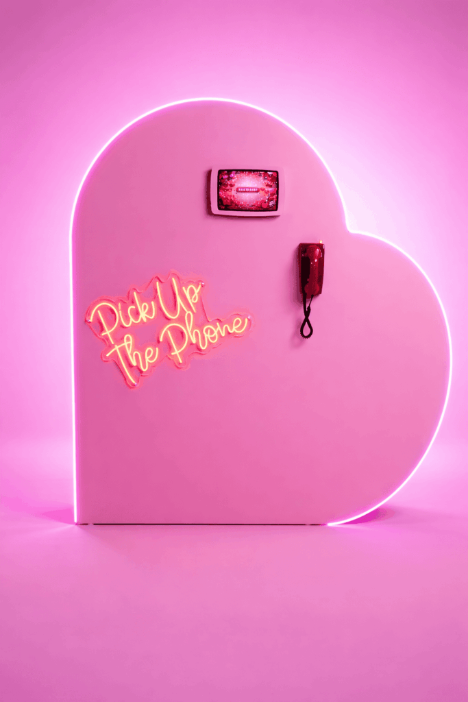 Pink heart-shaped audio guest book with a "Pick Up The Phone" neon sign, a screen and a red telephone handset